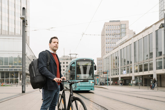 Entrepreneur with bicycle standing against cable car in city, Frankfurt, Germany