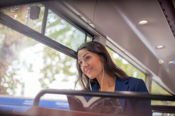 Young woman listening music on a bus with earphones, looking out of window