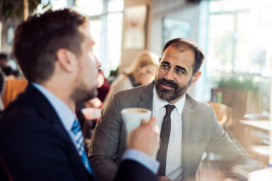 Middle aged man in formal suit talking to colleague in cafe