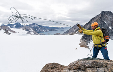 Greenland, Sermersooq, Kulusuk, Schweizerland Alps, mountaineer on summit throwing rope