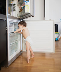 Fototapeta na wymiar Baby boy wearing diaper exploring refrigerator in the kitchen