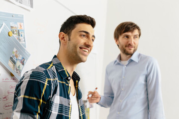 Two smiling colleagues at whiteboard in office - obrazy, fototapety, plakaty