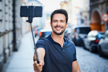 Man taking photo with smartphone mounted on selfie stick - obrazy, fototapety, plakaty