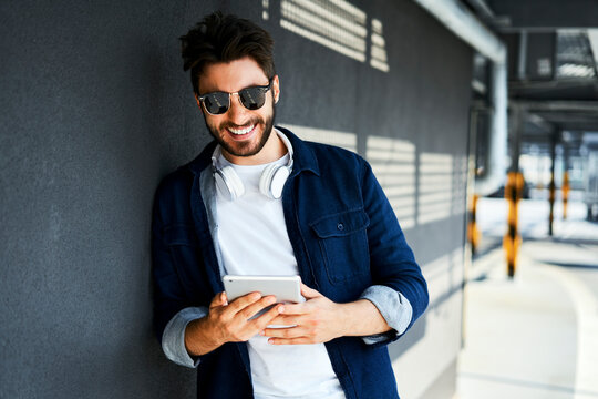 Portrait of smiling young man leaning against wall looking at digital tablet