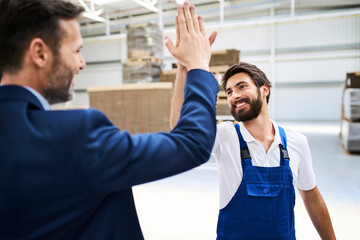 Happy businessman and worker high fiving in a factory