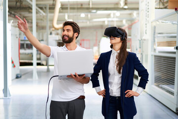 Man with laptop and businesswoman wearing VR glasses in factory