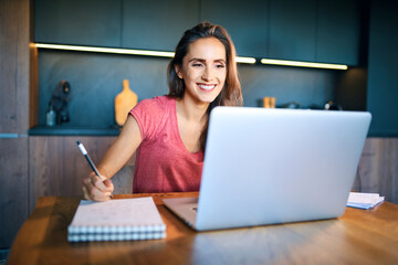 Smiling female entrepreneur looking at laptop while writing in note pad on desk