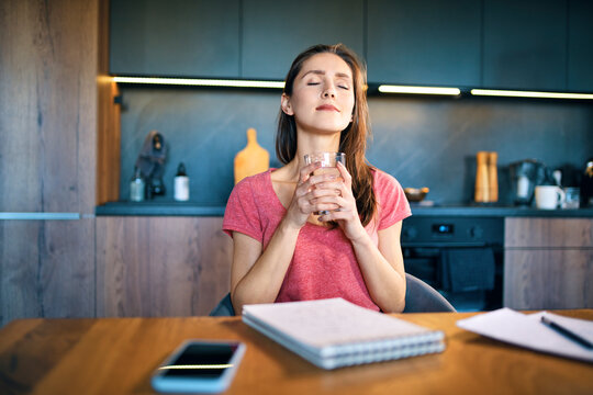 Smiling Female Entrepreneur With Eyes Closed Holding Drinking Glass At Desk In Home Office