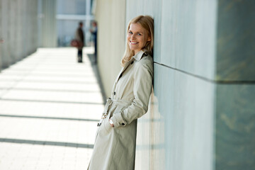 Portrait of smiling blond woman wearing trench coat leaning against facade