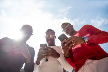 Three cool young men using cell phones in backlight