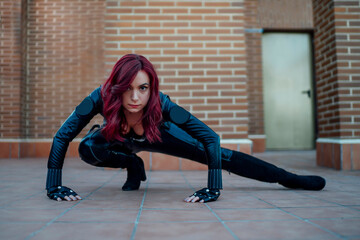 Portrait of redheaded woman wearing black leather catsuit crouching on rooftop