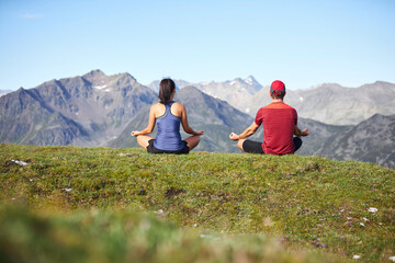Man and woman meditating in the mountains, rear view