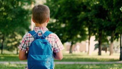 Tired schoolboy proceeds to educational institution on sunny day across park