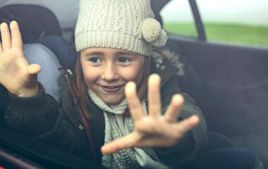 Portrait of happy little girl with wool cap putting her fingers on car window