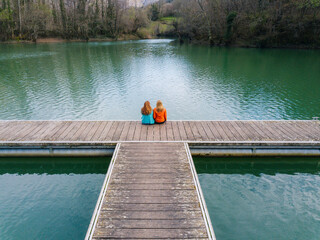 Back view of two friends sitting side by side on jetty, Valdemurio Reservoir, Asturias, Spain