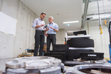 Two businessmen in factory hall with tyres examining product