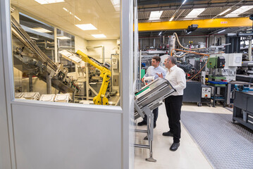Two men talking in factory shop floor looking at industrial robot