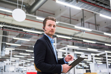 Man with headset in factory shop floor taking notes