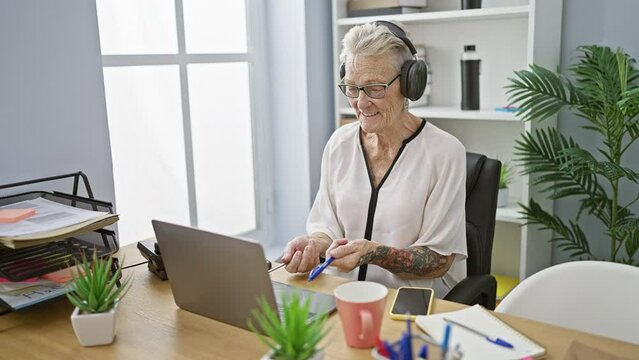 Jovial senior grey-haired business woman tapping into the rhythm at work, gleefully drumming her desk, enjoying music in office