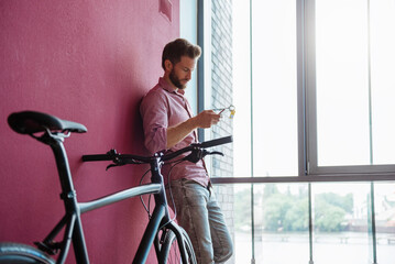 Man with bicycle standing in modern office looking at cell phone
