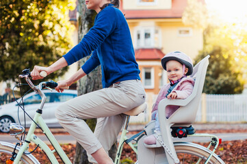 Mother and daughter riding bicycle, baby wearing helmet sitting in children's seat