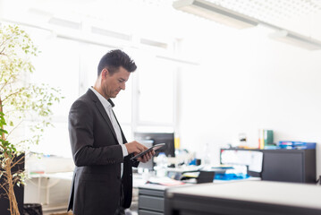 Fototapeta na wymiar Successful businessman standing in office, using digital tablet