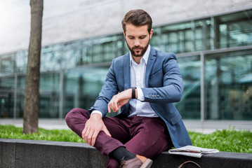 Young businessman sitting outdoors checking the time