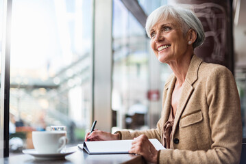 Smiling senior businesswoman taking notes in a cafe - obrazy, fototapety, plakaty