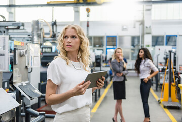 Woman holding tablet in factory shop floor with two women in background
