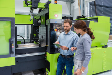 Colleagues in high tech company controlling manufacturing machines, using digital tablet