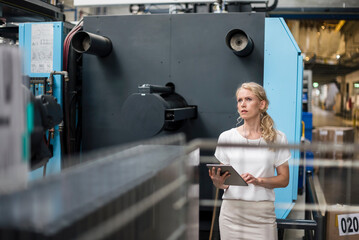 Woman with tablet at machine in factory shop floor looking around