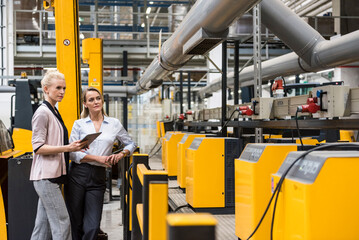 Two women with tablet looking at machine in factory shop floor