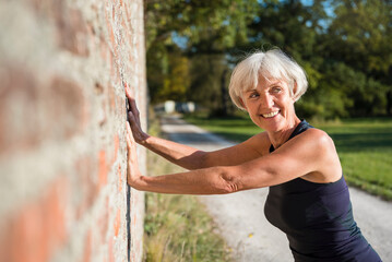 Smiling sportive senior woman leaning against a brick wall