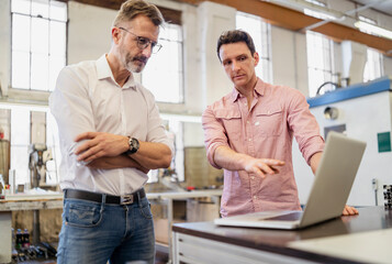 Two colleagues in factory discussing at laptop
