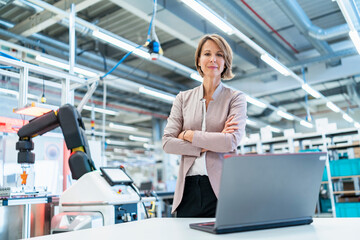 Portrait of confident businesswoman with laptop in a modern factory hall