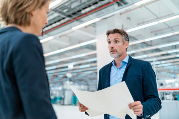 Businessman and businesswoman discussing plan in a factory hall