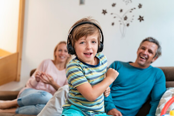 Portrait of boy listening to music with headphones on couch at home with parents in background