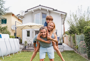 Portrait of father carrying wife and son piggyback in garden