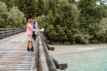 Young couple on a hiking trip reading map on wooden bridge, Vorderriss, Bavaria, Germany