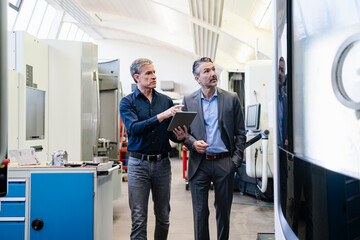 Businessmen in factory, having a meeting, using digital tablet