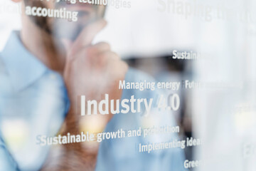 Businessman with hand on chin in front of glass pane with words, industry 4.0