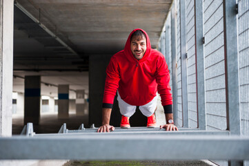 Portrait of happy young man doing push-ups in a car park