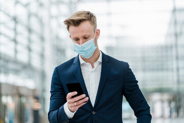 Businessman using smart phone while wearing face mask in city