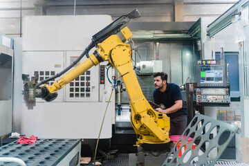 Young male worker analyzing robotic arm in manufacturing factory