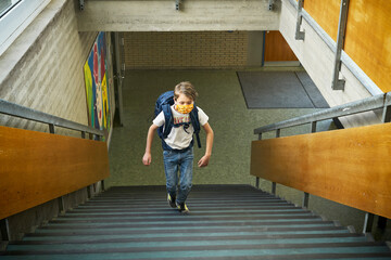 Boy wearing mask in school walking up stairs