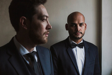 Gay couple in suits standing against wall on wedding day