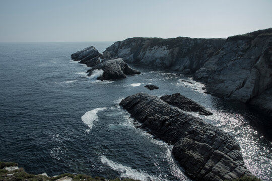 a rocky coastline with the ocean and cliffs in the background, taken from a high vantage point on a sunny day