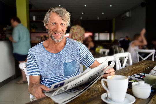 Portrait of smiling mature man sitting in a coffee shop reading newspaper - Powered by Adobe