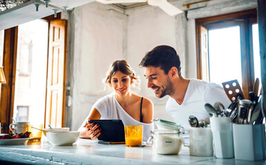 Young couple watching tablet while having breakfast at home