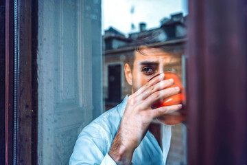 Young man holding cup looking out of window